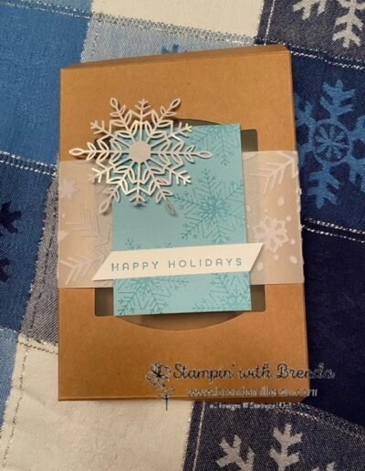 Kraft gift box with window wrapped with snowflake vellum and snowflake tag in blue and white with Happy Holidays