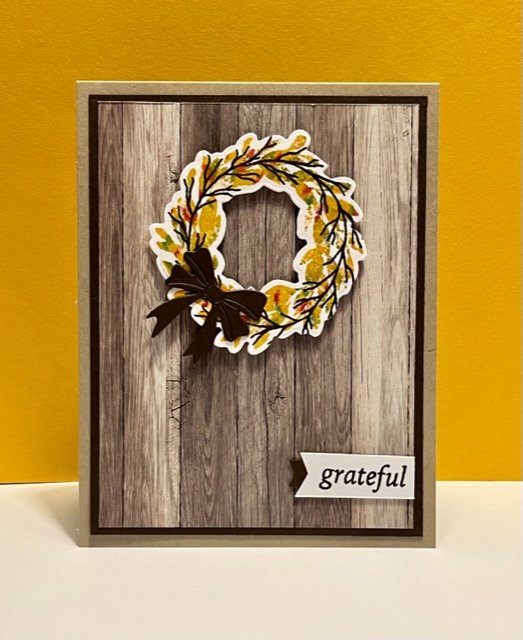 Woodgrain background with green, brown and yellow wreath with a bow, grateful sentiment
